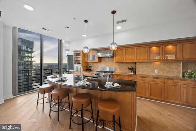 kitchen with sink, hanging light fixtures, an island with sink, and wall chimney exhaust hood