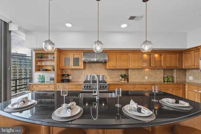 kitchen with pendant lighting, wall chimney range hood, decorative backsplash, and a center island with sink