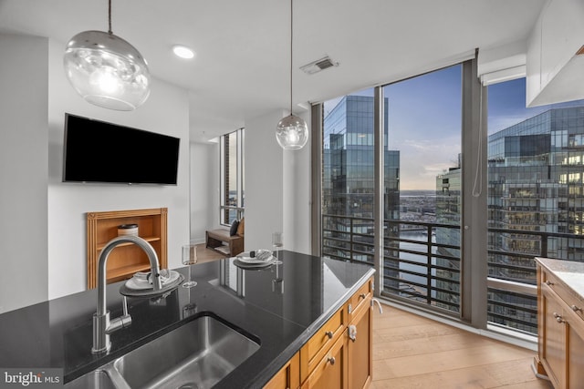 kitchen featuring expansive windows, decorative light fixtures, sink, and light hardwood / wood-style flooring