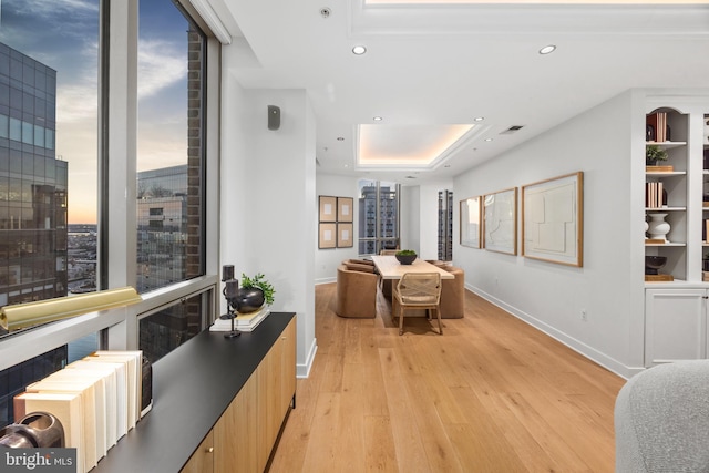 dining area with a wall of windows, a tray ceiling, and light wood-type flooring