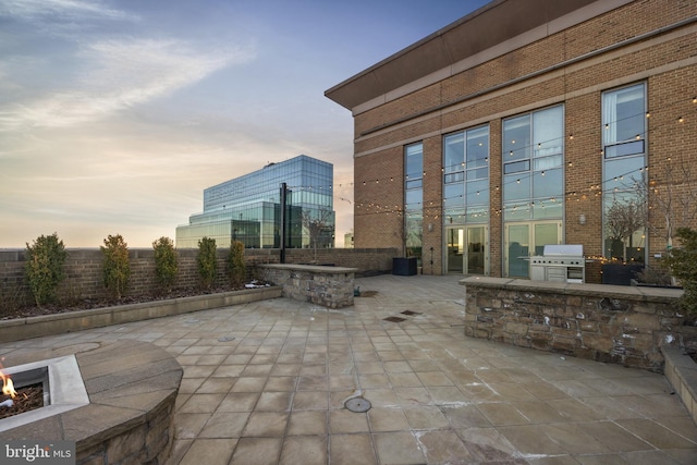 patio terrace at dusk with a grill, a fire pit, and an outdoor kitchen