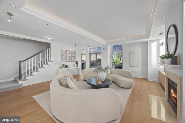 living room featuring light wood-type flooring, a high end fireplace, and a tray ceiling