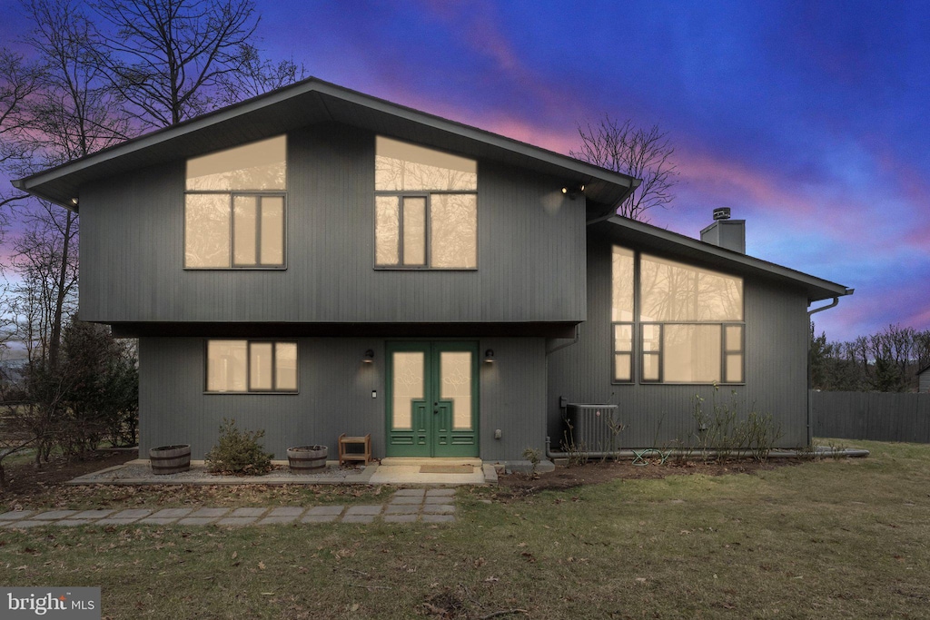 back house at dusk with french doors, a yard, and central AC unit