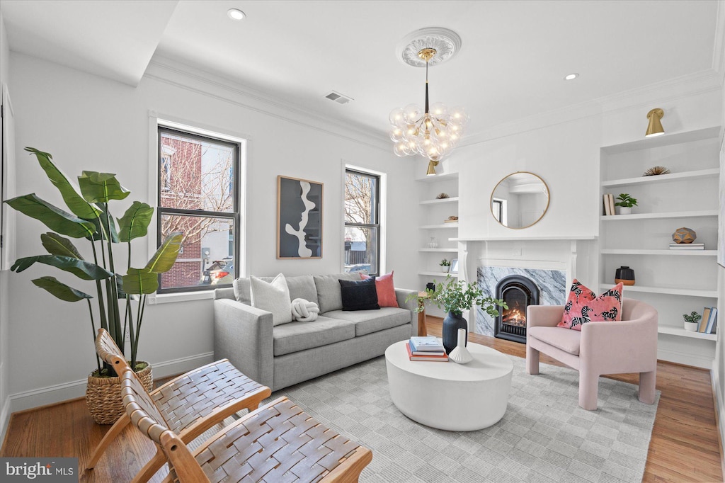 living room featuring an inviting chandelier, crown molding, a fireplace, and light hardwood / wood-style floors