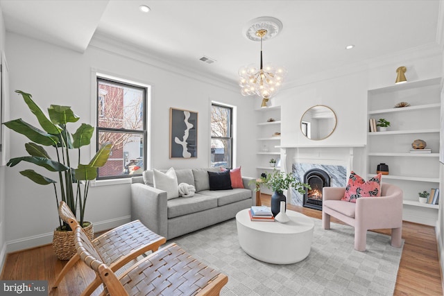 living room featuring an inviting chandelier, crown molding, a fireplace, and light hardwood / wood-style floors