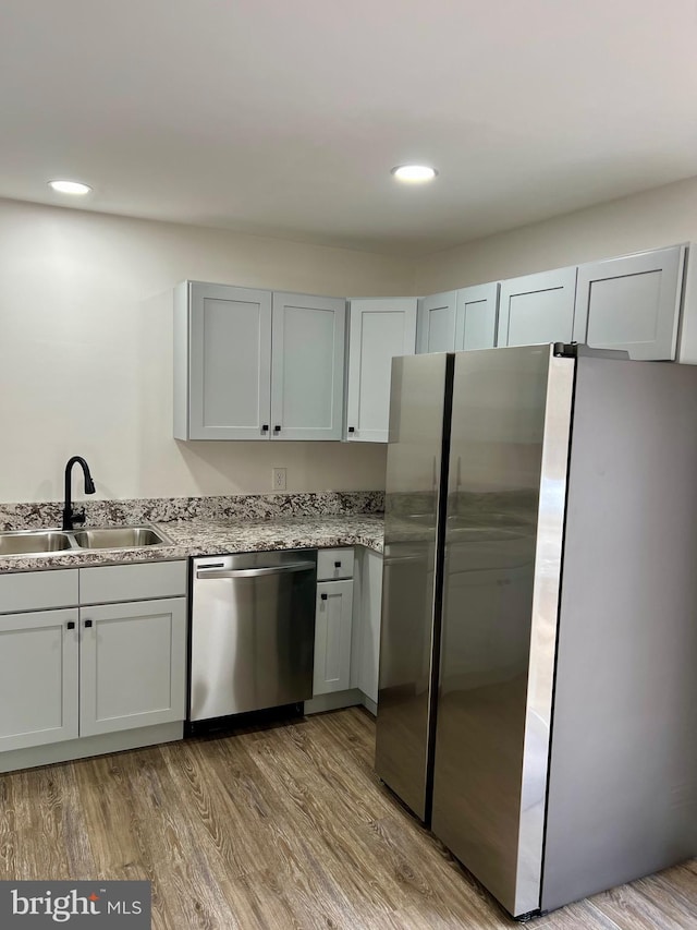 kitchen with sink, stainless steel appliances, light stone countertops, and light wood-type flooring