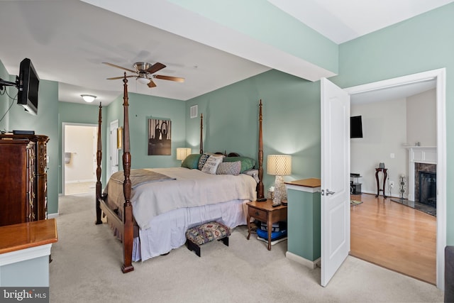 bedroom with light carpet, a fireplace, and ceiling fan