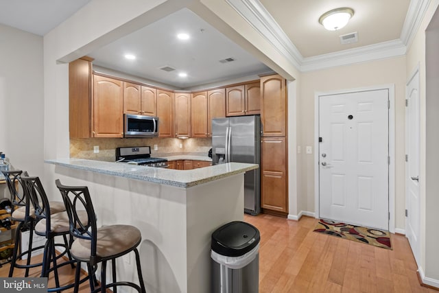 kitchen with backsplash, a kitchen bar, light hardwood / wood-style floors, kitchen peninsula, and stainless steel appliances