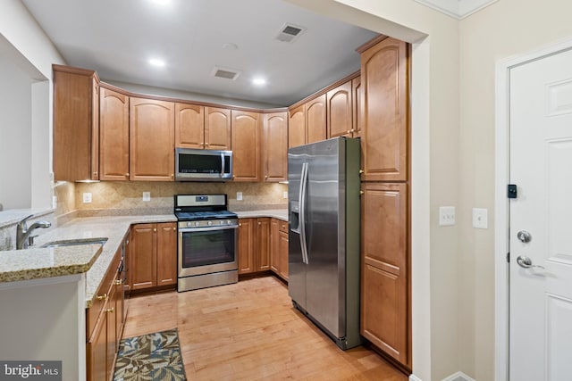 kitchen featuring stainless steel appliances, backsplash, light stone counters, and light hardwood / wood-style flooring