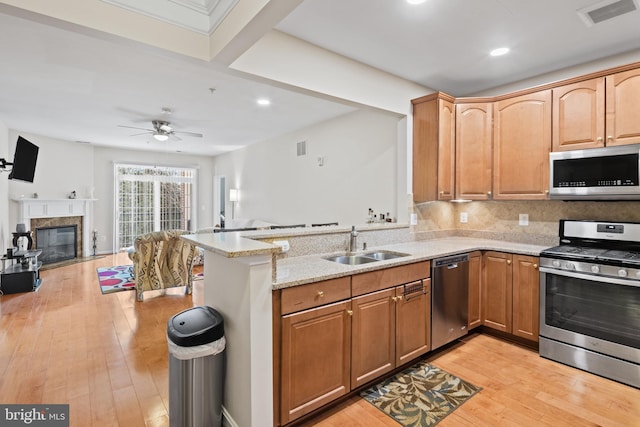 kitchen with sink, light wood-type flooring, kitchen peninsula, stainless steel appliances, and light stone countertops