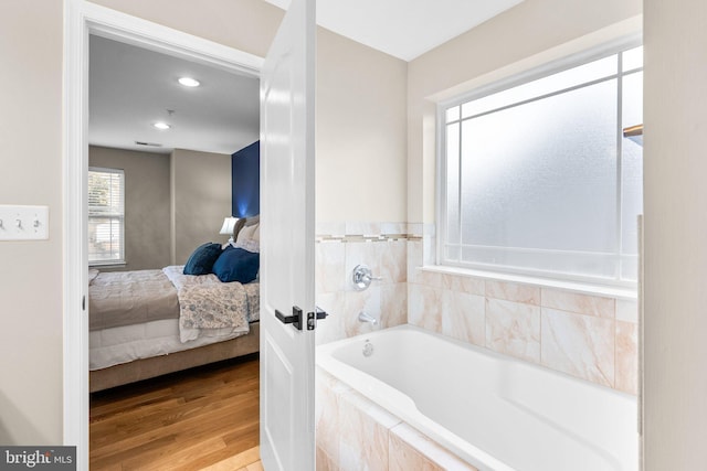 bathroom featuring tiled tub and wood-type flooring