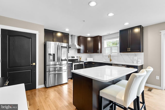 kitchen with appliances with stainless steel finishes, sink, a breakfast bar area, a center island, and wall chimney range hood