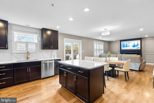 kitchen featuring sink, a kitchen bar, a center island, stainless steel dishwasher, and light hardwood / wood-style flooring