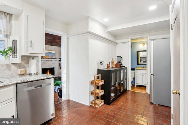 kitchen featuring appliances with stainless steel finishes, white cabinetry, decorative backsplash, crown molding, and a brick fireplace