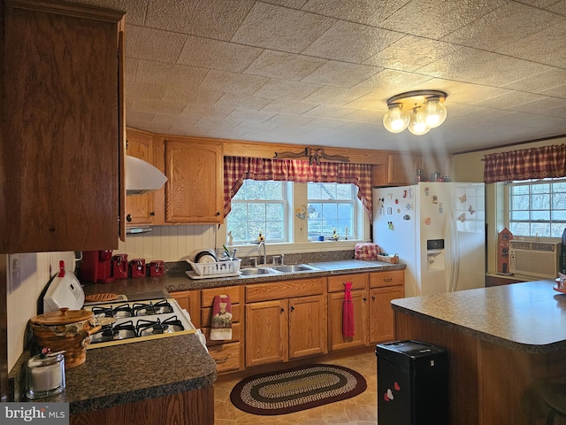 kitchen with white appliances, brown cabinetry, dark countertops, ventilation hood, and a sink