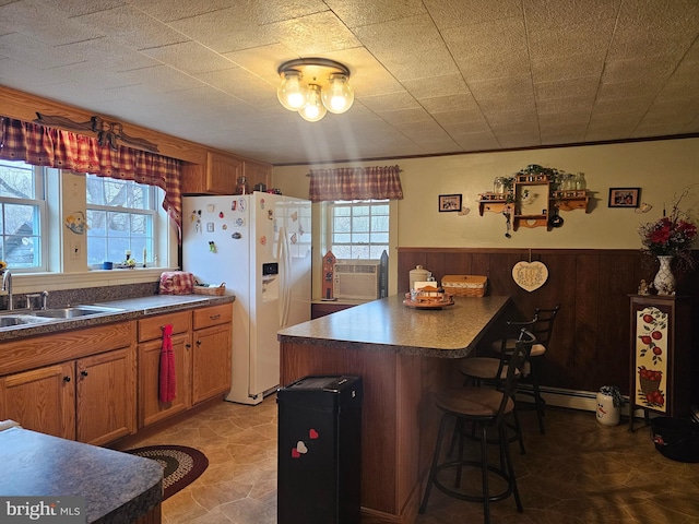 kitchen with brown cabinetry, dark countertops, a center island, white fridge with ice dispenser, and a sink