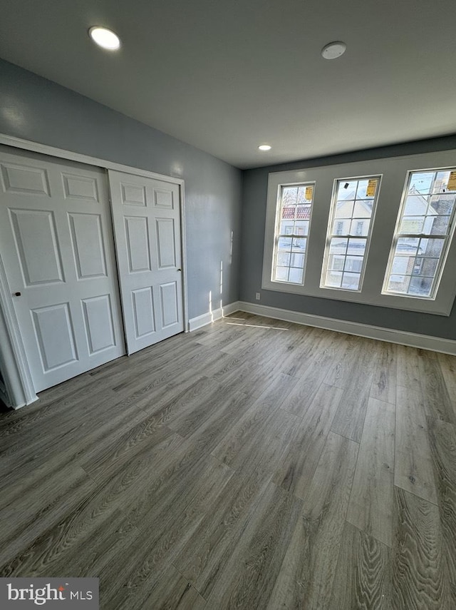 unfurnished bedroom featuring hardwood / wood-style flooring, a closet, and multiple windows