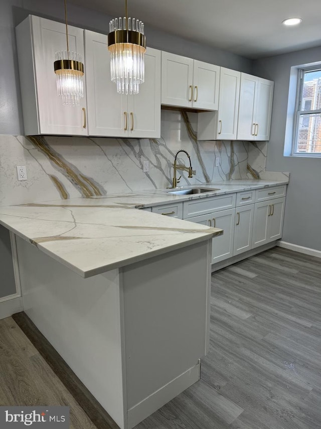 kitchen featuring white cabinetry, light stone countertops, sink, and pendant lighting