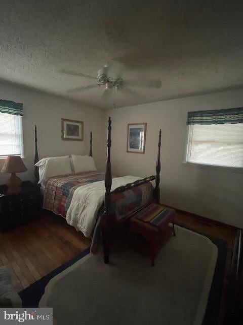 bedroom featuring ceiling fan, wood-type flooring, multiple windows, and a textured ceiling