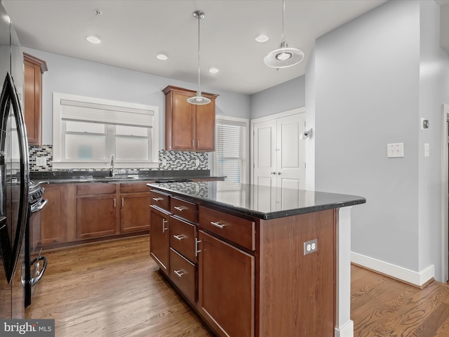 kitchen with decorative light fixtures, black refrigerator, a kitchen island, dark stone counters, and hardwood / wood-style floors