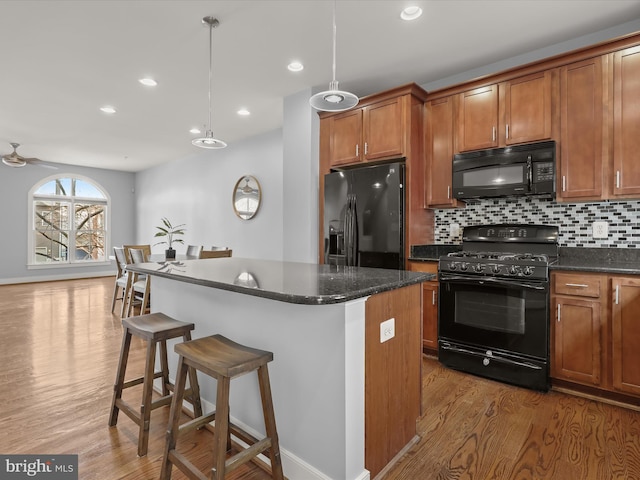 kitchen featuring a kitchen island, tasteful backsplash, dark hardwood / wood-style flooring, hanging light fixtures, and black appliances