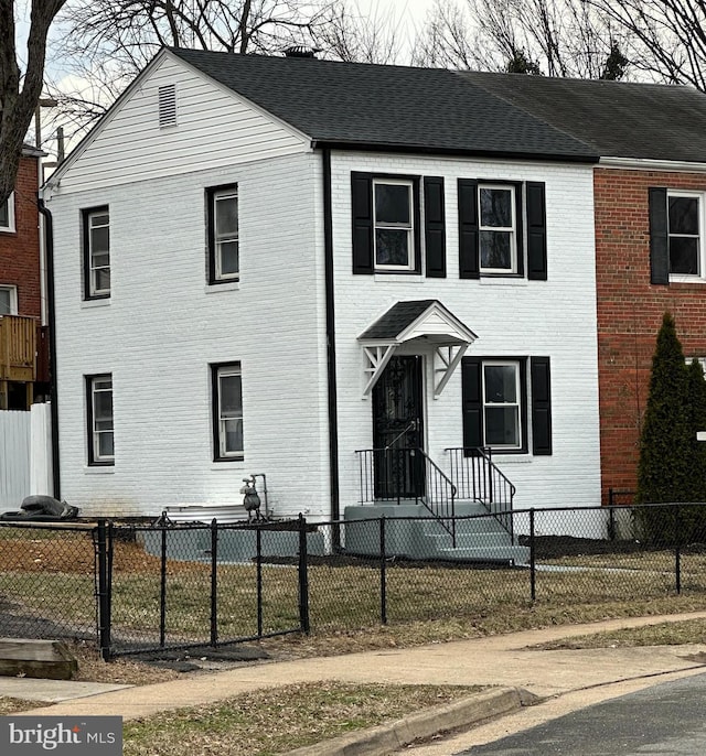 view of front of home with brick siding, a fenced front yard, and a shingled roof