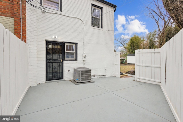 exterior space featuring a patio area, fence, central AC unit, and brick siding