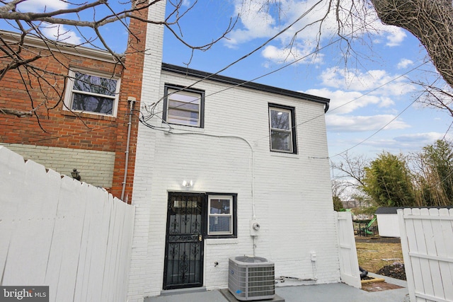 back of house featuring brick siding, a chimney, cooling unit, and fence