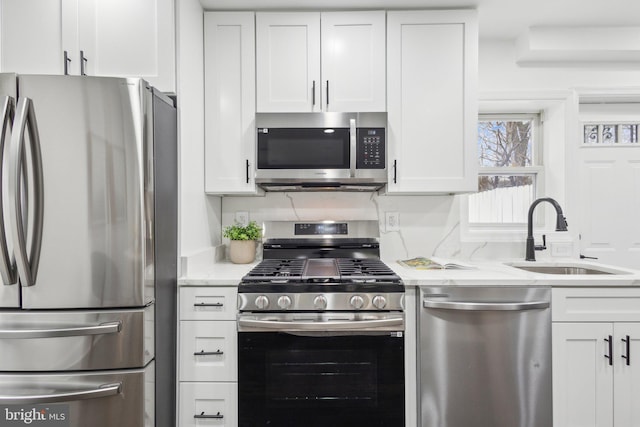 kitchen with stainless steel appliances, a sink, white cabinetry, and light stone countertops