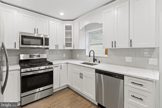 kitchen featuring sink, stainless steel appliances, light stone countertops, light hardwood / wood-style floors, and white cabinets