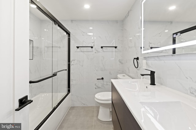 full bathroom featuring tile walls, vanity, toilet, and combined bath / shower with glass door