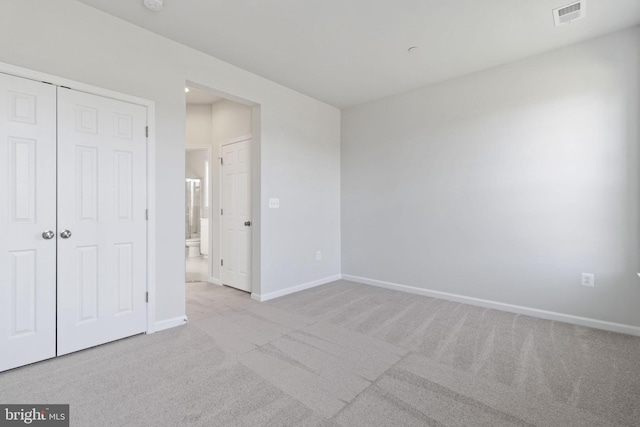 unfurnished bedroom with connected bathroom, light colored carpet, and a closet