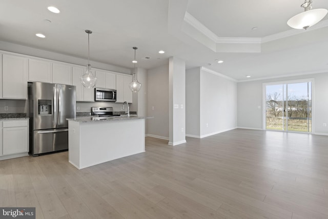 kitchen with pendant lighting, white cabinets, stainless steel appliances, a center island with sink, and light hardwood / wood-style flooring