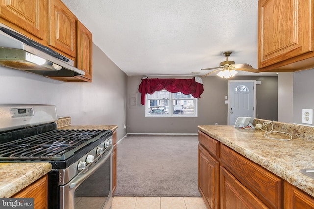 kitchen with stainless steel gas range oven, light carpet, ceiling fan, and a textured ceiling