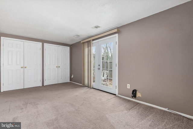 unfurnished bedroom with a textured ceiling, access to outside, light colored carpet, french doors, and multiple closets