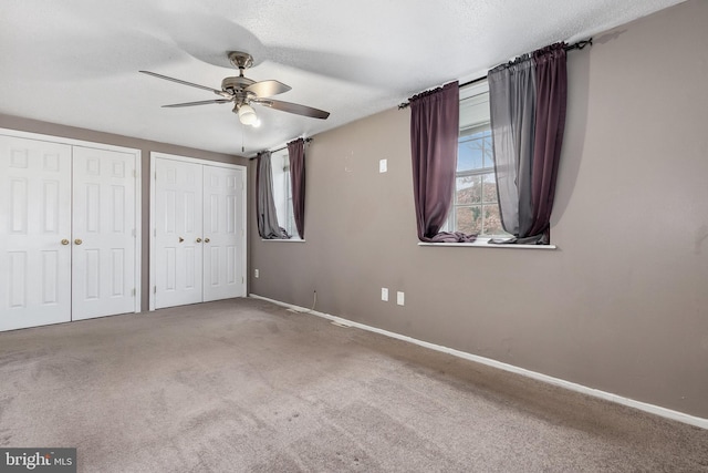 unfurnished bedroom with multiple closets, carpet flooring, a textured ceiling, and ceiling fan