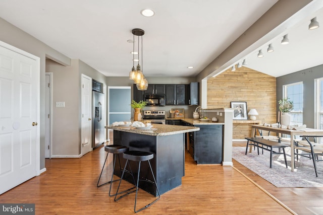 kitchen featuring a breakfast bar, appliances with stainless steel finishes, wooden walls, light hardwood / wood-style floors, and decorative light fixtures