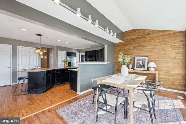 dining room with vaulted ceiling, light wood-type flooring, and wood walls