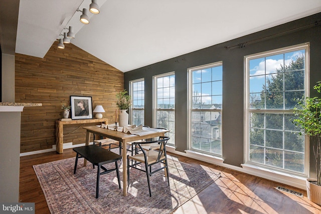 dining space with lofted ceiling, hardwood / wood-style floors, track lighting, and wood walls