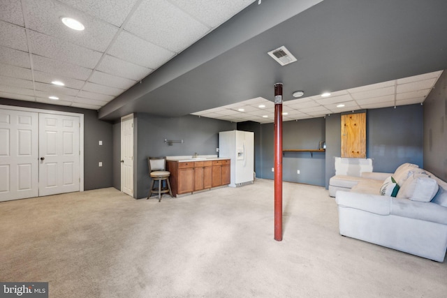 interior space featuring white fridge with ice dispenser, light carpet, a drop ceiling, and indoor wet bar