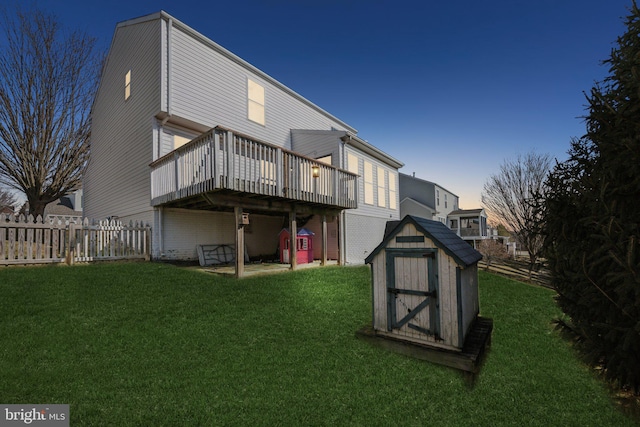 back house at dusk with a wooden deck, a storage unit, and a lawn