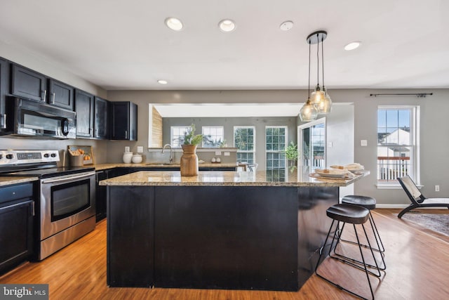 kitchen with sink, light stone counters, stainless steel electric range oven, hanging light fixtures, and a kitchen island