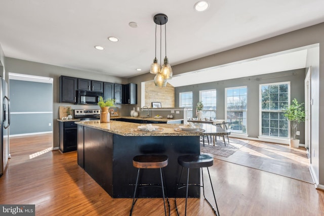 kitchen featuring appliances with stainless steel finishes, a breakfast bar, hanging light fixtures, a center island, and light stone countertops