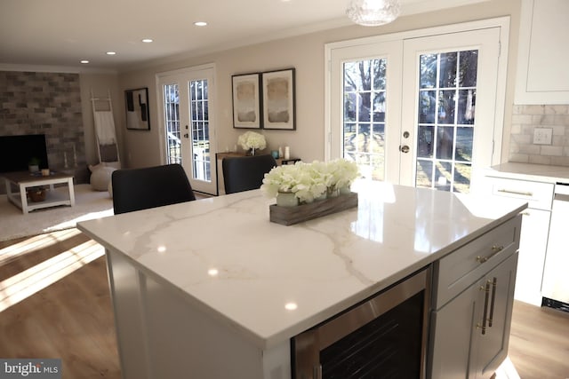 kitchen with wine cooler, ornamental molding, light stone countertops, and french doors