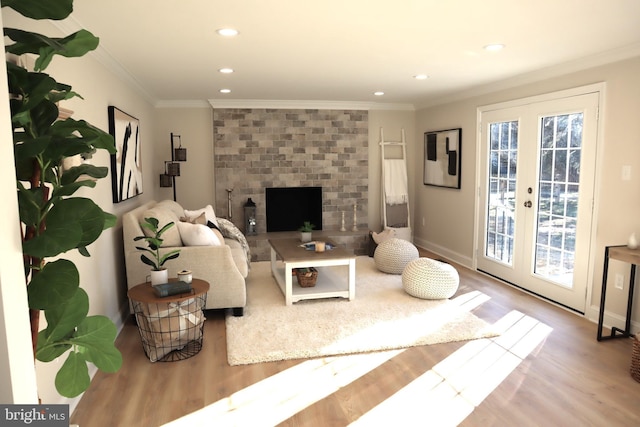 living room with ornamental molding, a brick fireplace, light hardwood / wood-style floors, and french doors