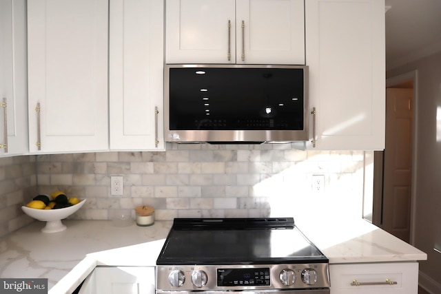 kitchen with stainless steel appliances, light stone countertops, white cabinets, and decorative backsplash