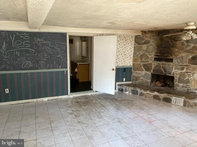 unfurnished living room with ceiling fan, a stone fireplace, and a textured ceiling