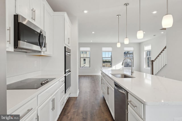 kitchen with decorative light fixtures, white cabinetry, sink, stainless steel appliances, and a center island with sink