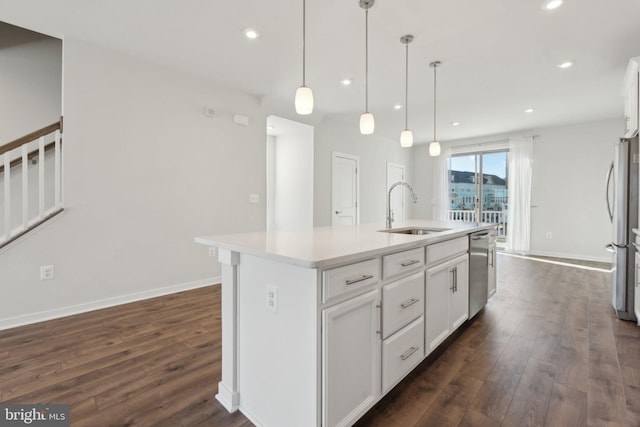 kitchen featuring an island with sink, sink, white cabinets, hanging light fixtures, and stainless steel appliances