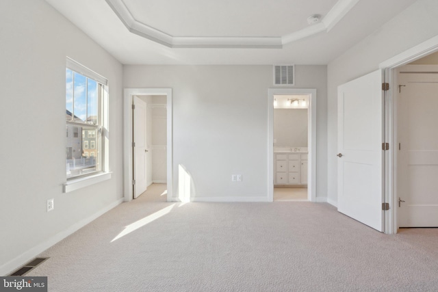 unfurnished bedroom with light colored carpet, a raised ceiling, and a walk in closet